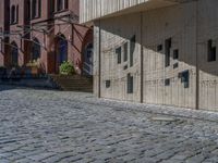 cobblestone driveway surrounded by modern buildings on sunny day with sun reflecting onto the windows