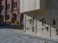 cobblestone driveway surrounded by modern buildings on sunny day with sun reflecting onto the windows