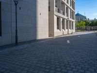 two people walking down an empty city street in an alley area with tall buildings in the background