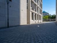 two people walking down an empty city street in an alley area with tall buildings in the background