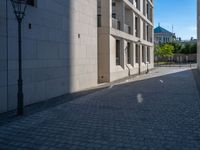 two people walking down an empty city street in an alley area with tall buildings in the background