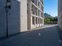 two people walking down an empty city street in an alley area with tall buildings in the background