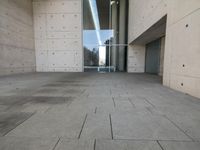 a woman on the street looking down at an empty floor near a building with a wall behind her