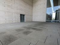 a woman on the street looking down at an empty floor near a building with a wall behind her