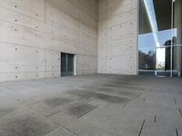 a woman on the street looking down at an empty floor near a building with a wall behind her