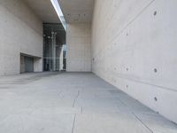 a woman on the street looking down at an empty floor near a building with a wall behind her