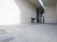 a woman on the street looking down at an empty floor near a building with a wall behind her