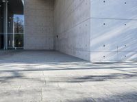 a woman on the street looking down at an empty floor near a building with a wall behind her