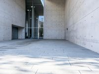 a woman on the street looking down at an empty floor near a building with a wall behind her