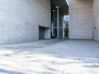 a woman on the street looking down at an empty floor near a building with a wall behind her