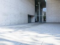 a woman on the street looking down at an empty floor near a building with a wall behind her