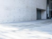 a woman on the street looking down at an empty floor near a building with a wall behind her