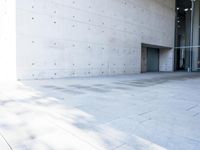 a woman on the street looking down at an empty floor near a building with a wall behind her