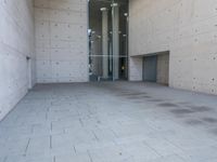 a woman on the street looking down at an empty floor near a building with a wall behind her