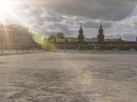 the sun is coming through the clouds above a plaza and buildings overlooking water and sky