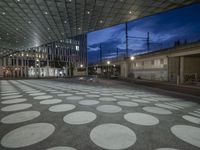 an empty concrete plaza in front of a glassy building at night time with illuminated dots