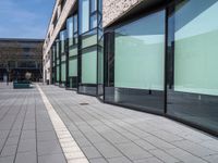 an empty sidewalk next to the glassed buildings in the city with people walking around