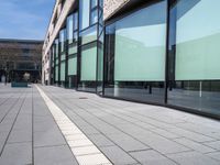 an empty sidewalk next to the glassed buildings in the city with people walking around