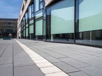 an empty sidewalk next to the glassed buildings in the city with people walking around