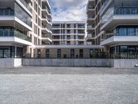 three tall building near the concrete fence and a parking lot with a bench near one of the buildings