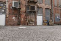 a man sits on a skateboard in front of an old brick building with several doors