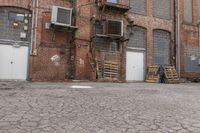 a man sits on a skateboard in front of an old brick building with several doors