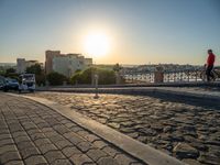 the sun setting in the distance over a town street with cars parked next to it