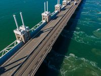 a bridge over the ocean with construction equipment in the background and two people walking on it