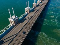 a bridge over the ocean with construction equipment in the background and two people walking on it