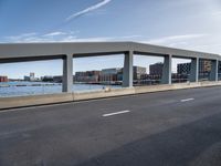 a long, concrete walkway along a river that goes through some buildings, which also have cars on it