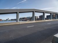 a long, concrete walkway along a river that goes through some buildings, which also have cars on it