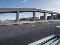 a long, concrete walkway along a river that goes through some buildings, which also have cars on it