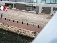 there is a sign on a bricked walkway by the water with people walking on the side