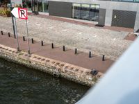 there is a sign on a bricked walkway by the water with people walking on the side