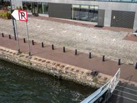 there is a sign on a bricked walkway by the water with people walking on the side