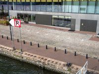 there is a sign on a bricked walkway by the water with people walking on the side