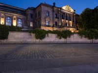 a building that is near a road with bushes in it at night with lights on