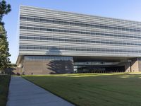 an open air building with grass and trees in front of it with an outside walkway leading up to the front