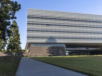 an open air building with grass and trees in front of it with an outside walkway leading up to the front