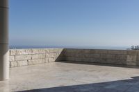a patio with stone columns and flooring facing the ocean, a building in the background