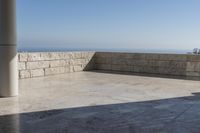 a patio with stone columns and flooring facing the ocean, a building in the background