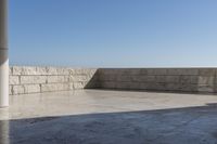 a patio with stone columns and flooring facing the ocean, a building in the background