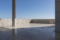 a patio with stone columns and flooring facing the ocean, a building in the background