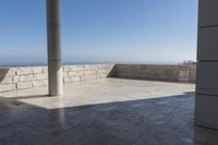 a patio with stone columns and flooring facing the ocean, a building in the background