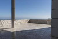 a patio with stone columns and flooring facing the ocean, a building in the background
