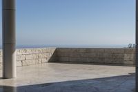 a patio with stone columns and flooring facing the ocean, a building in the background