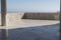 a patio with stone columns and flooring facing the ocean, a building in the background