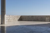 a patio with stone columns and flooring facing the ocean, a building in the background