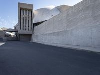 the view down a parking lot towards an abstract building with white stucco and light concrete walls