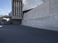 the view down a parking lot towards an abstract building with white stucco and light concrete walls